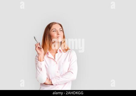 Young woman standing isolated on white background holding pen looking aside smiling pensive Stock Photo
