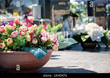 Cemetery in sunny day. Gravestone with flowers and candles. Grave decoration close-up. Graveyard in the daytime. Grave flowers in pot. Stock Photo