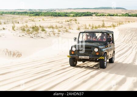 Mui Ne, Vietnam - June 2019: off-road vintage soviet car driving through desert sand dunes at sunrise. Stock Photo