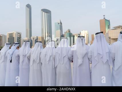 Arabic men standing in traditional cloth around modern buildings - Middle Eastern Culture - Emirati Men performing Al Ayala traditional dance Stock Photo