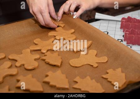 female hands spread the dough in the shape of a man on baking paper. The process of making Christmas cookies. Selective focus. Stock Photo