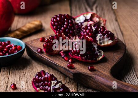 Fresh ripe whole pomegranates,  opened pomegranate  and  seeds in bowl, knife on wooden board, still life, close up Stock Photo