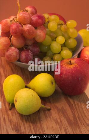 A plate with grapes and some apples and pears scattered on a wooden table Stock Photo