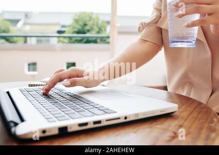 Young woman with glass of water checking data on laptop screen Stock Photo
