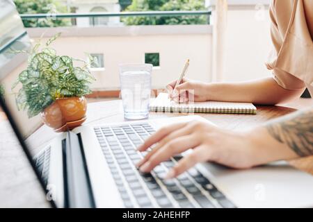 Hands of female student watching webinar on laptop and taking notes in textbook Stock Photo