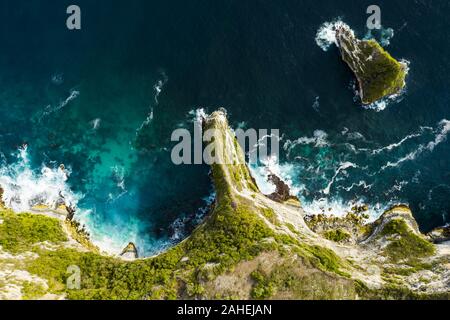 View from above, stunning aerial view of a green limestone cliff bathed by a turquoise sea during sunset. Nusa Penida, Indonesia. Stock Photo