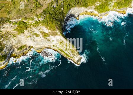 View from above, stunning aerial view of a green limestone cliff bathed by a turquoise sea during sunset. Nusa Penida, Indonesia. Stock Photo