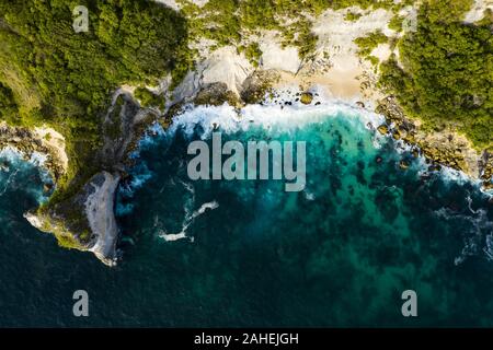 View from above, stunning aerial view of a green limestone cliff with a beautiful wild beach bathed by a turquoise sea. Nusa Penida, Indonesia. Stock Photo