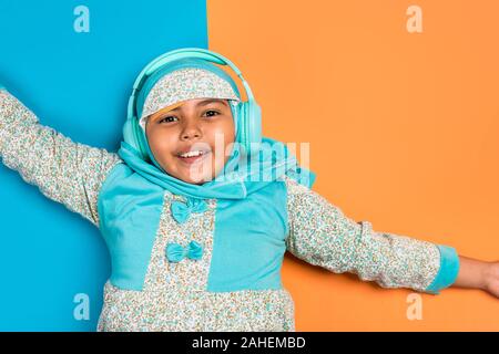 Young muslim Asian girl wearing hijab happily listening to music with headphones - Happy childhood bright and colorful concept image with copy space f Stock Photo