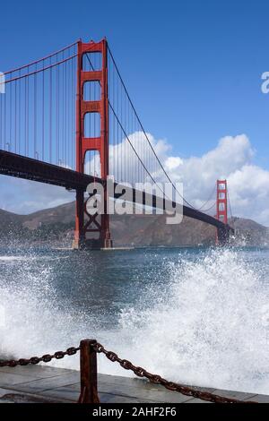International orange Golden Gate Bridge with waves breaking on to the embankment in front in San Francisco, United States of America Stock Photo