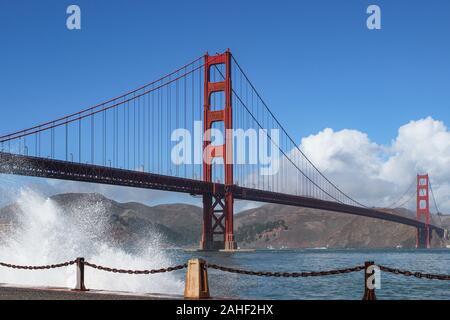 Waves breaking on to the embankment with international orange Golden Gate Bridge in background in San Francisco, United States of America Stock Photo