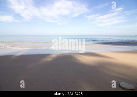 The calm sea on a wonderful sandy beach flows into the bright sunny sky Stock Photo