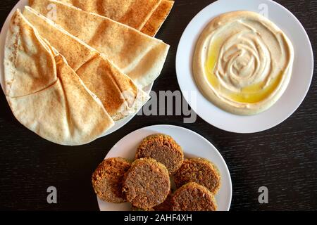 Famous traditional Arabic, Middle East, Israel cuisine. Tahini sauce, pita bread and falafel on dark wooden background. Flat lay, top view. Stock Photo