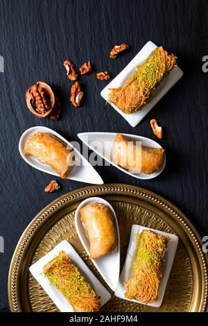 Food concept Oriental arab dessert baklava walnuts and rolled Kanafeh on black slate board with copy space Stock Photo