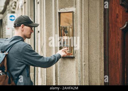 A guy or a man or a tourist presses a doorphone button to access inside. Stock Photo