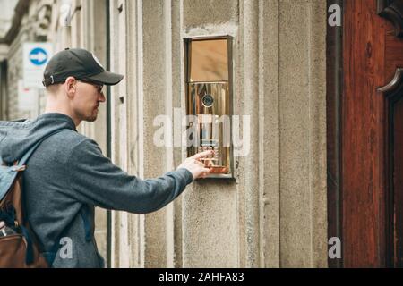 A guy or a man or a tourist presses a doorphone button to access inside. Stock Photo