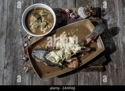 Deep fried whole Snakehad fish topped with Acacia omelets in vegetable sour soup (Orange curry with Cha-om). Stock Photo