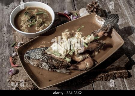 Deep fried whole Snakehad fish topped with Acacia omelets in vegetable sour soup (Orange curry with Cha-om). Stock Photo