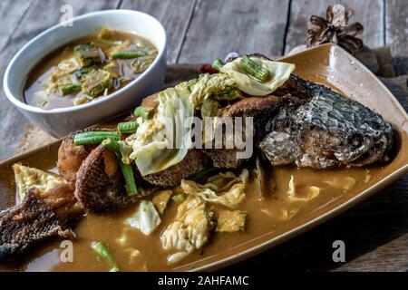 Deep fried whole Snakehad fish topped with Acacia omelets in vegetable sour soup (Orange curry with Cha-om). Stock Photo