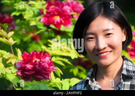 A smiling chinese woman with a flowering tree peony background in Jingshan Park beijing china. Stock Photo