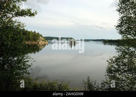 Scenery of summer season showing small island in the middle of the lake, trees, water, lake, clouds, sky, foliage, in its tranquility environment. Stock Photo