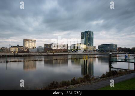 Überseestadt in Bremen, Germany with reflections on the river Weser and lights in the office buildings during blue houer with cloudy sky Stock Photo