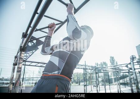 Waist up of young man doing chin ups on the bar outdoors Stock Photo
