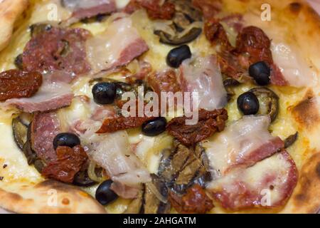 Close up on bacon pizza with dried tomatoes, cheese and black olives. From top. Fast food concept Stock Photo