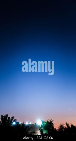 Venus and crescent Moon visible in the evening sky at dusk above farmhouse in Kabd, Kuwait - Dec 27, 2019 Stock Photo