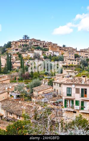 Amazing cityscape of the small coastal village Deia in Mallorca, Spain. Typical houses located in terraces on the hill surrounded by green trees. Spanish tourist attraction. Vertical photo. Stock Photo