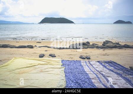 Two beach sarongs and flip flops on sand by shore on calm empty sea at sunset in the island of Koh Phangan, Thailand. Couple gone swimming Stock Photo
