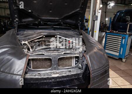 Disassembled black car with opene hood in the workshop raised on the lift prepared for repair, internal equipment, parts and spare parts visible. Auto Stock Photo