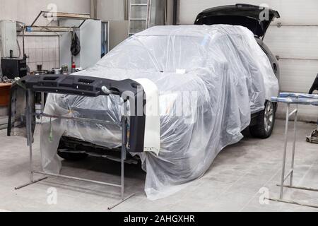Auto bumper part is installed on the racks after painting in the car repair shop in the room with tools and equipment for repairing body parts after a Stock Photo
