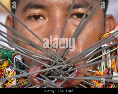 Thai Chinese Taoist devotee (mah song) pierces his cheeks and lips with decorated steel pins/skewers during the Phuket Vegetarian Festival. Stock Photo