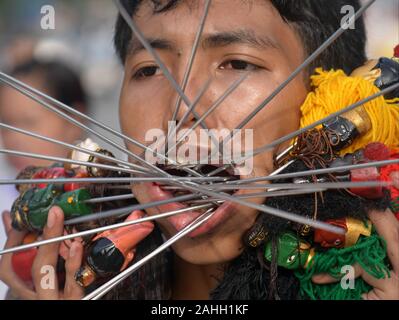 Young Thai Chinese Taoist devotee (mah song, masong) pierces his cheeks with decorated steel pins/skewers during the Vegetarian Festival. Stock Photo