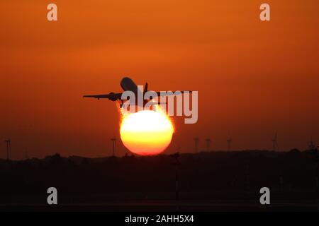 Plane taking off into the sunset with a few windturbines in the background Stock Photo