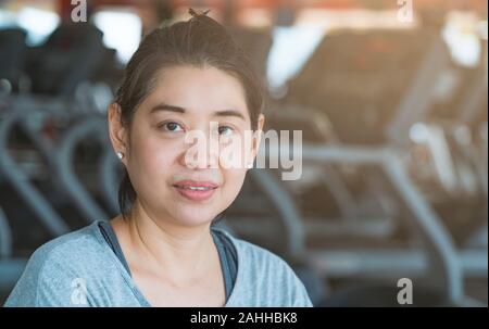 Portrait of Asian mother or middle-aged woman with blurred gym background. Model is gentle looks, little bit sweats and looking at camera. Stock Photo