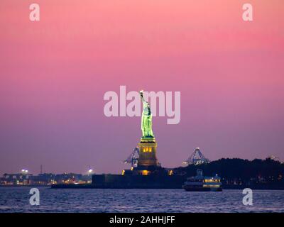 Liberty island, New York City - Statue of Liberty on Hudson river during cruise sunset at dusk Stock Photo