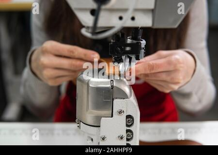 Sewing machine in a leather workshop in action with hands working on a leather details for shoes. Women's hands with sewing machine at shoes factory. Stock Photo