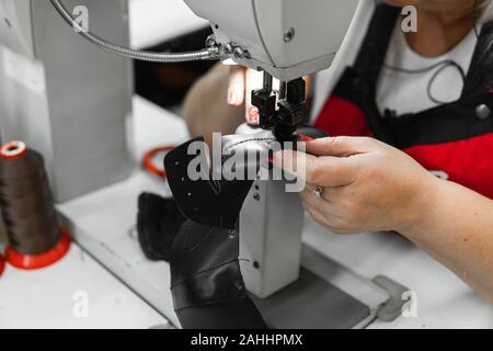 Sewing machine in a leather workshop in action with hands working on a leather details for shoes. Women's hands with sewing machine at shoes factory. Stock Photo