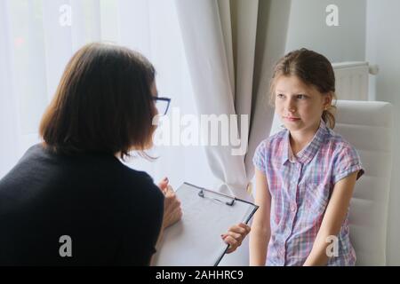 Woman social worker psychologist talking to girl child in office, female counselor taking notes in clipboard. Children mental health Stock Photo