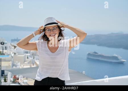 Portrait of middle aged woman traveling on luxury cruise in Mediterranean. Smiling female looking at camera on Santorini island, copy space