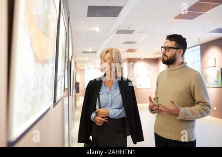 Waist up portrait of mature couple looking at paintings while enjoying exhibition in art gallery or museum, copy space Stock Photo