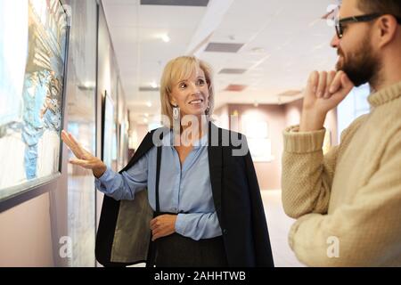 Waist up portrait of cheerful mature couple standing by paintings while enjoying exhibition in art gallery or museum Stock Photo