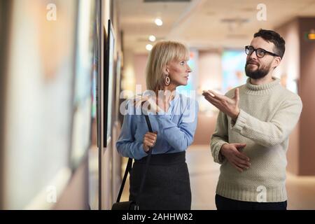 Waist up portrait of modern mature couple looking at paintings while enjoying exhibition in art gallery or museum, copy space Stock Photo