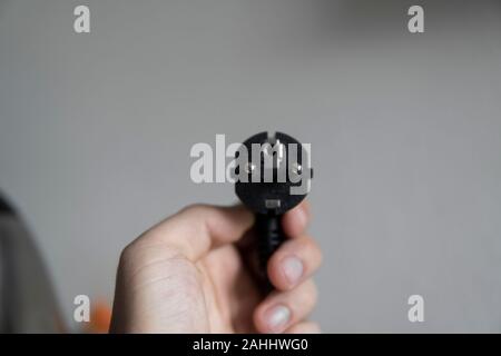 Hand holding black electric plug on a grey background. Stock Photo