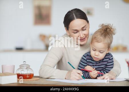 Portrait of mature mother drawing with little girl while enjoying time together at home, copy space Stock Photo