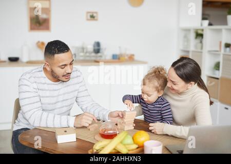 Portrait of happy mixed-race family playing with cute little daughter while enjoying breakfast at home, copy space Stock Photo