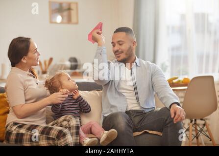 Warm toned portrait of happy modern family playing with cute little girl in cozy home interior, copy space