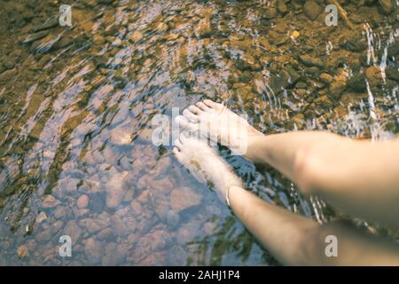 in the memory, woman put feet in water, have stone under river with reflection Stock Photo